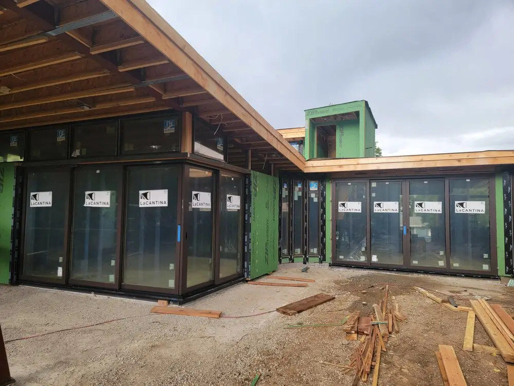 Alt Text: Modern Colorado home under construction featuring large folding glass doors, contemporary architecture, and a blog graphic titled "Big Glass Doors for Colorado Homes: The Complete 2026 Guide."